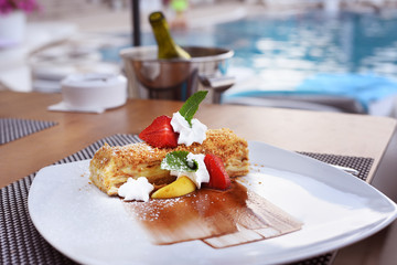 Ukrashenny puff cake with fruit and whipped cream on the table near the pool. Very appetizing dessert.