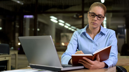 Fototapeta premium Young businesswoman writing startup ideas into notebook, planning meeting