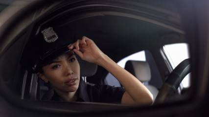 Fototapeta na wymiar Asian police officer adjusting her uniform cap looking into rearview mirror