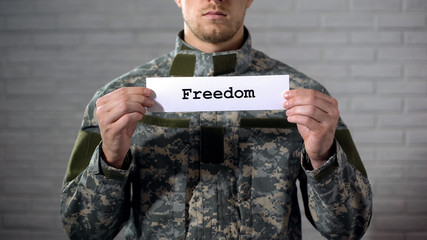 Freedom word written on sign in hands of male soldier, peace, end of war