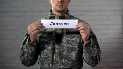 Justice word written on sign in hands of male soldier, military court, tribunal