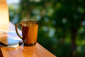 Cup of coffee and cellphone on the windowsill over blurred forest background at sunny summer day. Free copy space.