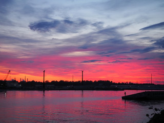 A beautiful red and yellow sunset over the city is reflected in the water of the river with the .silhouette of a fisherman in the background. Panoramic landscape on the dusk.