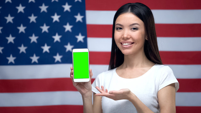 Girl showing smartphone with green screen, US flag on background, translator app - Powered by Adobe