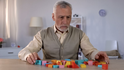 Sad pensioner looking at color building blocks on table, rehabilitation center