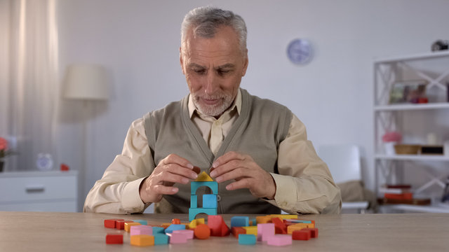 Positive old man playing with wooden cubes, cognitive training in Alzheimer