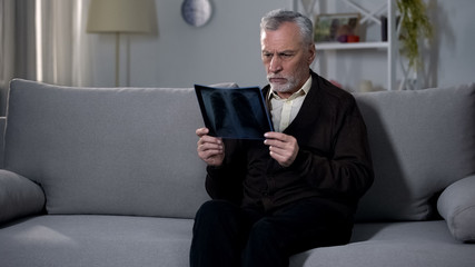 Old man sadly looking at x-ray image, difficulty coping with terminal diagnosis