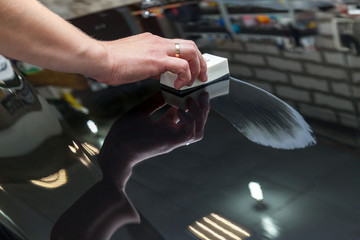 The process of applying a nano-ceramic coating on the car's hood by a male worker with a sponge and...