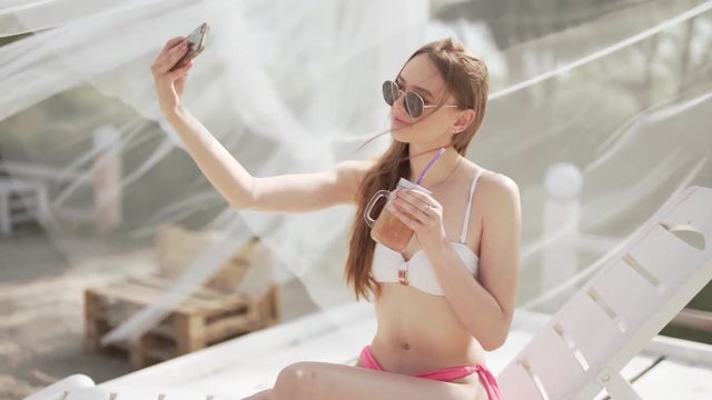 Young sexy girl in bikini clicking a selfie on a beach resort, medium close up