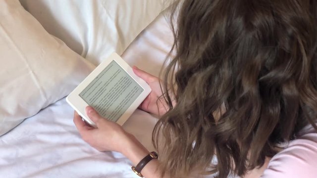 Girl lying on the bed reading an e-book, top view