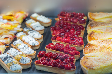 Colorful icing raspberry tart and fruit tart displayed in patisserie 