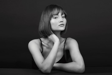 Fototapeta premium Beauty portrait of a beautiful young smiling girl with beautiful glowing skin and natural makeup on a black background in a black dress. Black and white portrait of a woman.