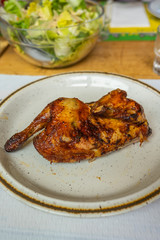 Crispy half roasted chicken on white plate in restaurant