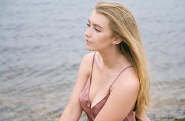 Young woman in pink dress sitting on sand and enjoys sea.