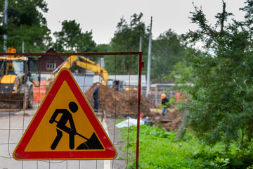 Road works sign on defocused background of workers and construction equipment