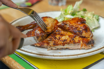 Human hand holding knife and fork and eating grilled chicken