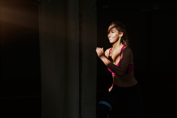 Young woman with fit body running against dark background. Female model in sportswear exercising outdoors.Woman Doing Workout Exercises On Street.