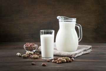Fresh peanut milk in glass and pitcher on dark wooden table. Rustic style.
