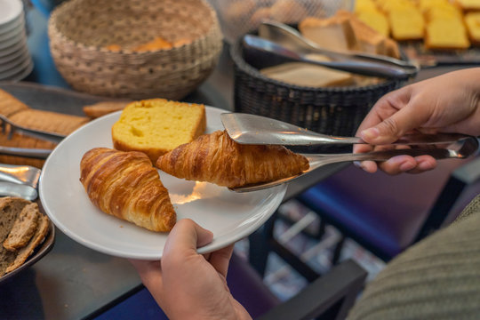 Woman picking croissant into a plate for breakfast in hotel