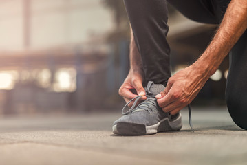 A single man tying his shoelaces, ready to start exercising for an upcoming marathon - obrazy, fototapety, plakaty