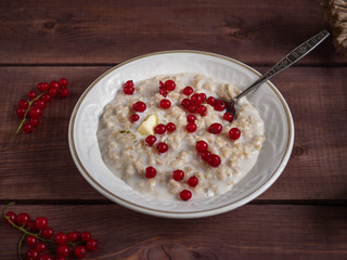 Oatmeal on milk with red currant in a white plate on a wooden tray