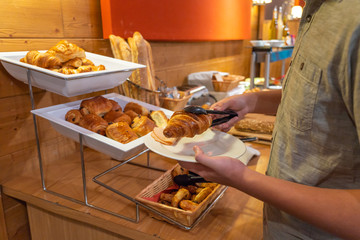 Asian man picking croissant into his plate at buffet meal