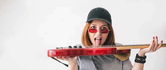 Young beautiful woman musician showing her toungue posing with red bass guitar on white background....