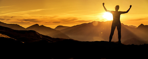 Frau in Siegerpose bei Sonnenaufgang auf einem Berggipfel