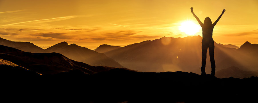 Frau in Siegerpose bei Sonnenaufgang auf einem Berggipfel