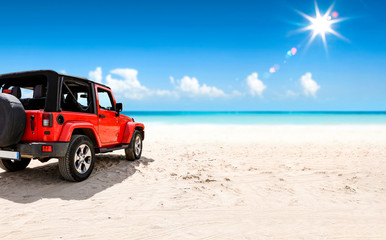 A red jeep on sandy beach and beuatiful blue sunny sky view in summer time. - obrazy, fototapety, plakaty