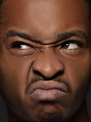 Close up portrait of young and emotional african-american man. Highly detail photoshot of male model with well-kept skin and bright facial expression. Concept of human emotions. Thinking with grimaces