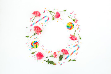 Frame of roses flowers with petals and sugar candy on white background. Flat lay, top view.