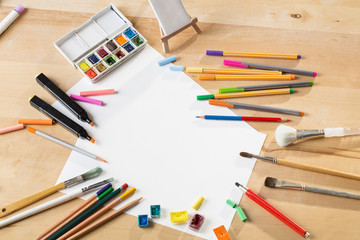 background with a set of watercolor paints, pencils, brushes and sheets of paper on a wooden table