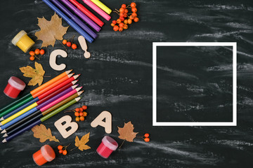 School concept. Colored pencils, dried maple leaves, rowan and white frame on black table background. Flat lay, top view, copy space.