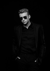young man with black glasses in black jacket on black background, black and white photo