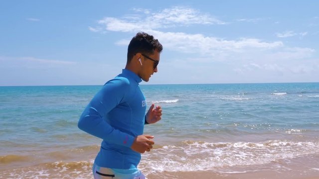 Athletic guy jogging along coast on a sunny day. Jogging outdoor near the sea. Concept healthy, active lifestyle.