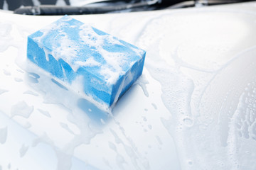 blue sponge and soap over the car for washing. Motor hood being cleaned. Concept car wash clean....