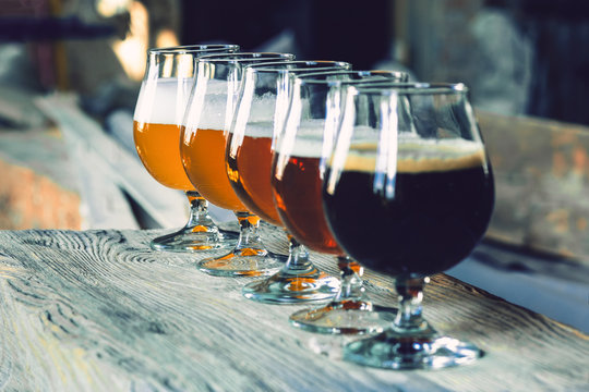 Glasses of different kinds of dark and light beer on wooden table in line. Cold delicious drinks are prepared for a big friend's party. Concept of drinks, fun, meeting, oktoberfest.