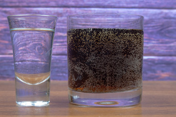 Vodka and cola in different glasses on a wooden table