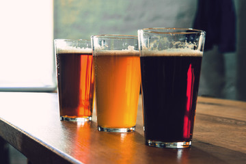 Glasses of different kinds of dark and light beer on wooden table in line. Cold delicious drinks are prepared for a big friend's party. Concept of drinks, fun, meeting, oktoberfest.