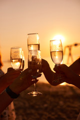 Happy young women drinking champagne at bachelorette party on the beach. Bride and bridesmaid...