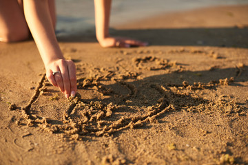 girl in love draws a heart on the sand by the sea