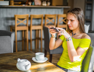 portrait of young teenager brunette girl with long hair sitting indoor in urban cafe and use her...