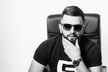 Fashion man posing.  Handsome young man looking at camera while sitting against white background. Success, business, young. Black and white.