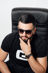 Perfect style. Young handsome man holding hand on chin and looking away while sitting.  Fashion man posing.