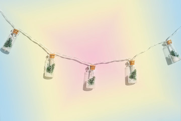 Light garland from small glass bottles with small Christmas trees inside on a neon background