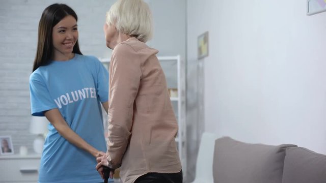Kind hospital volunteer helping disabled pensioner with walking stick, altruism