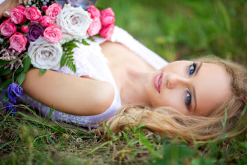 Obraz na płótnie Canvas beautiful young woman with make-up in a pink dress lies in the park on the grass with a bouquet of flowers