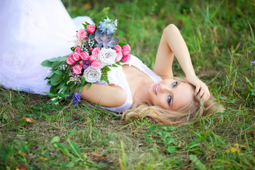 beautiful young woman with make-up in a pink dress lies in the park on the grass with a bouquet of flowers