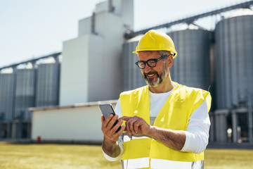 engineer using tablet in front of blurred grain silos